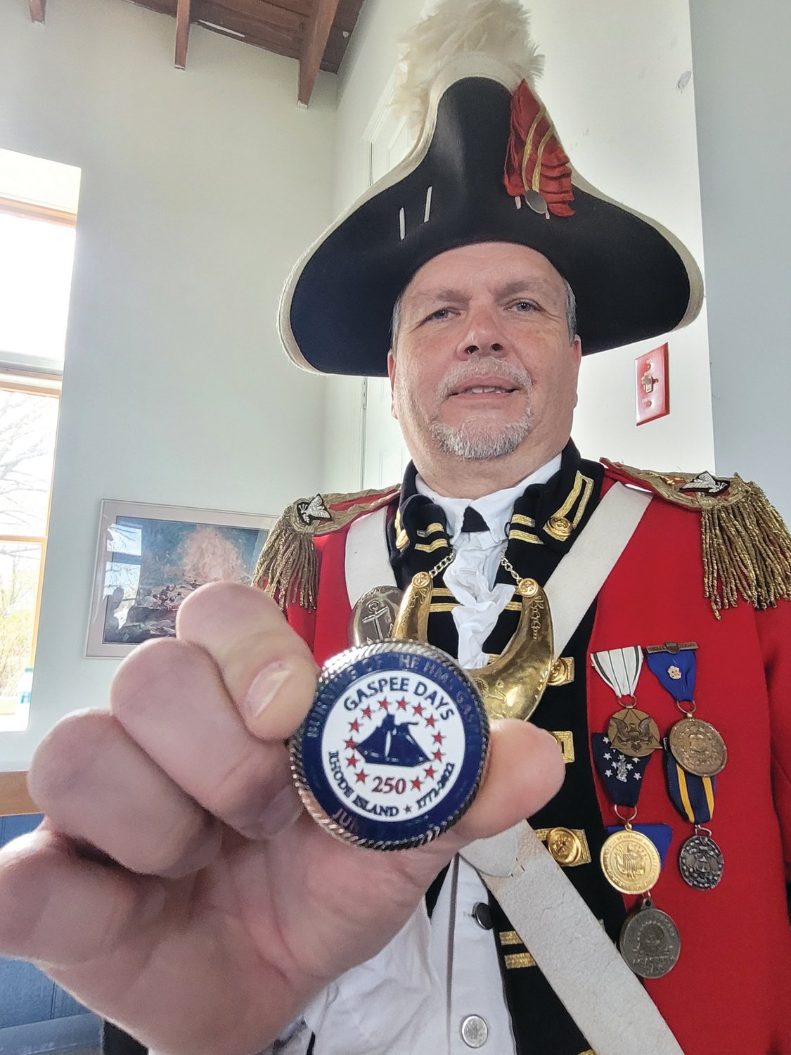 CHALLENGE COIN: Col. Ron Barnes, Commander of the Pawtuxet Rangers, holds a challenge coin. Barnes presented a similar coin to Britain’s Consul General for New England Dr. Peter Abbott OBE, during an announcement event for an underwater search for the Gaspee’s remains. If Barnes challenges Abbott to show the coin while out for drinks, and Abbott can’t produce it, the tab’s on the Brits. If he challenges and Abbott produces the coin, drinks are on the Pawtuxet Rangers.